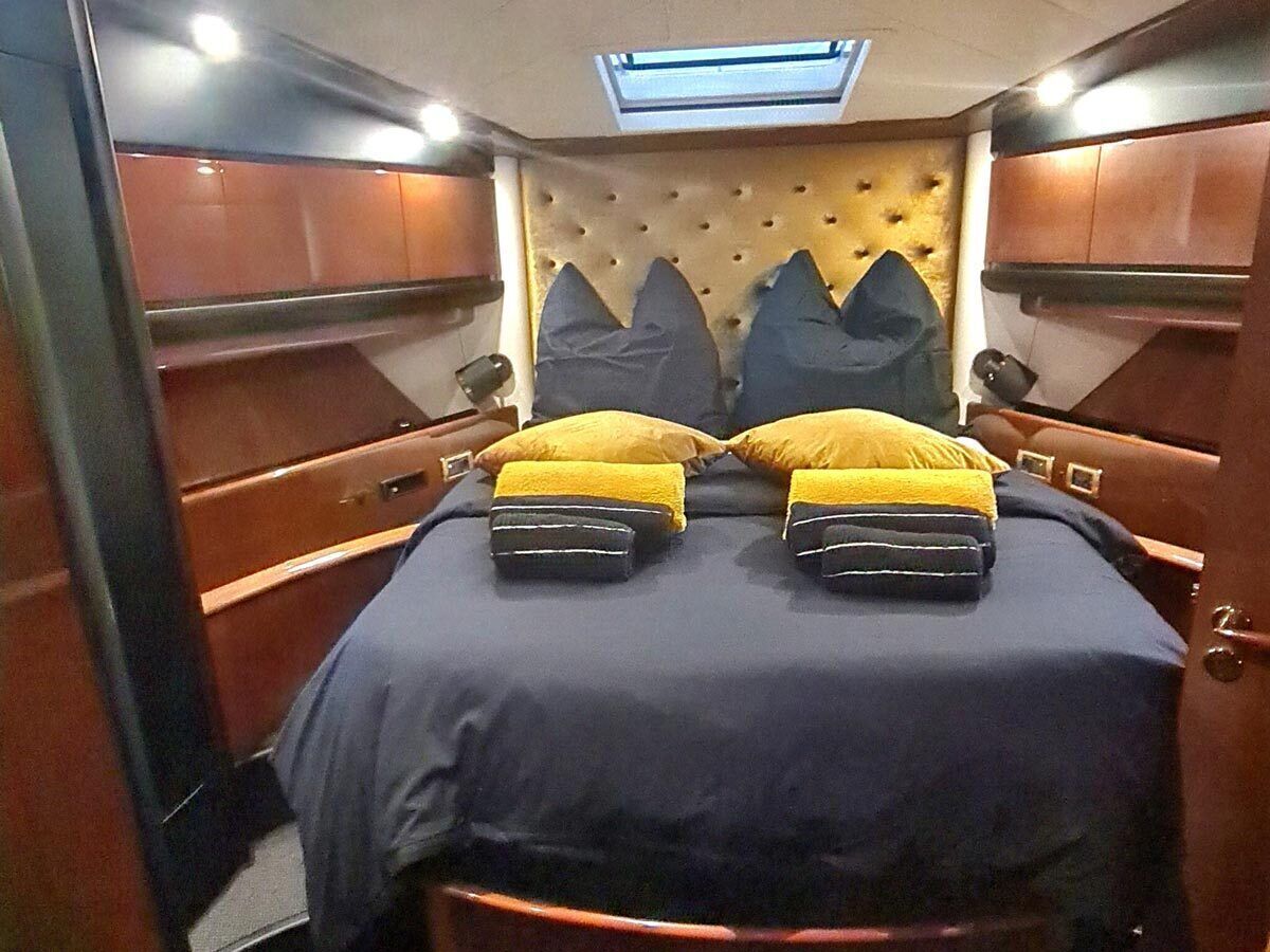A narrow, enclosed room with a bed, two pillows, a headboard, and a skylight.