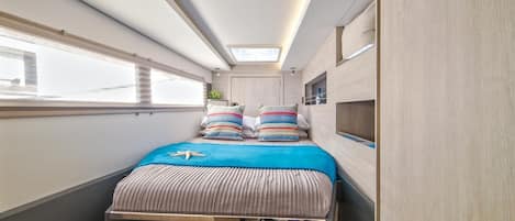 A narrow, well-lit room with a bed, a skylight, and a window.