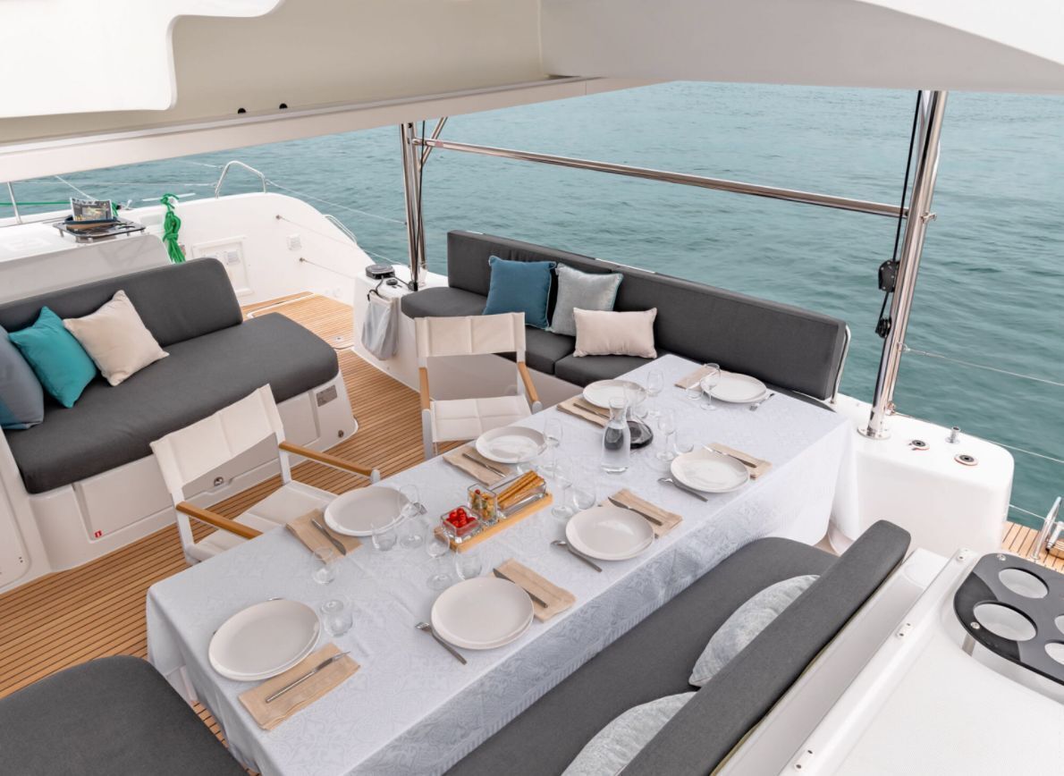 Un pont de bateau équipé d’une table à manger pour quatre personnes, d’un canapé et d’une petite table sur laquelle est posée une serviette verte.