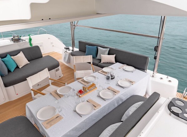 A boat deck with a dining table set for four, a sofa, and a small table with a green towel.