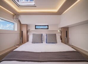 A modern bedroom with a skylight, a bed with two pillows, a bedside table, and a small window.
