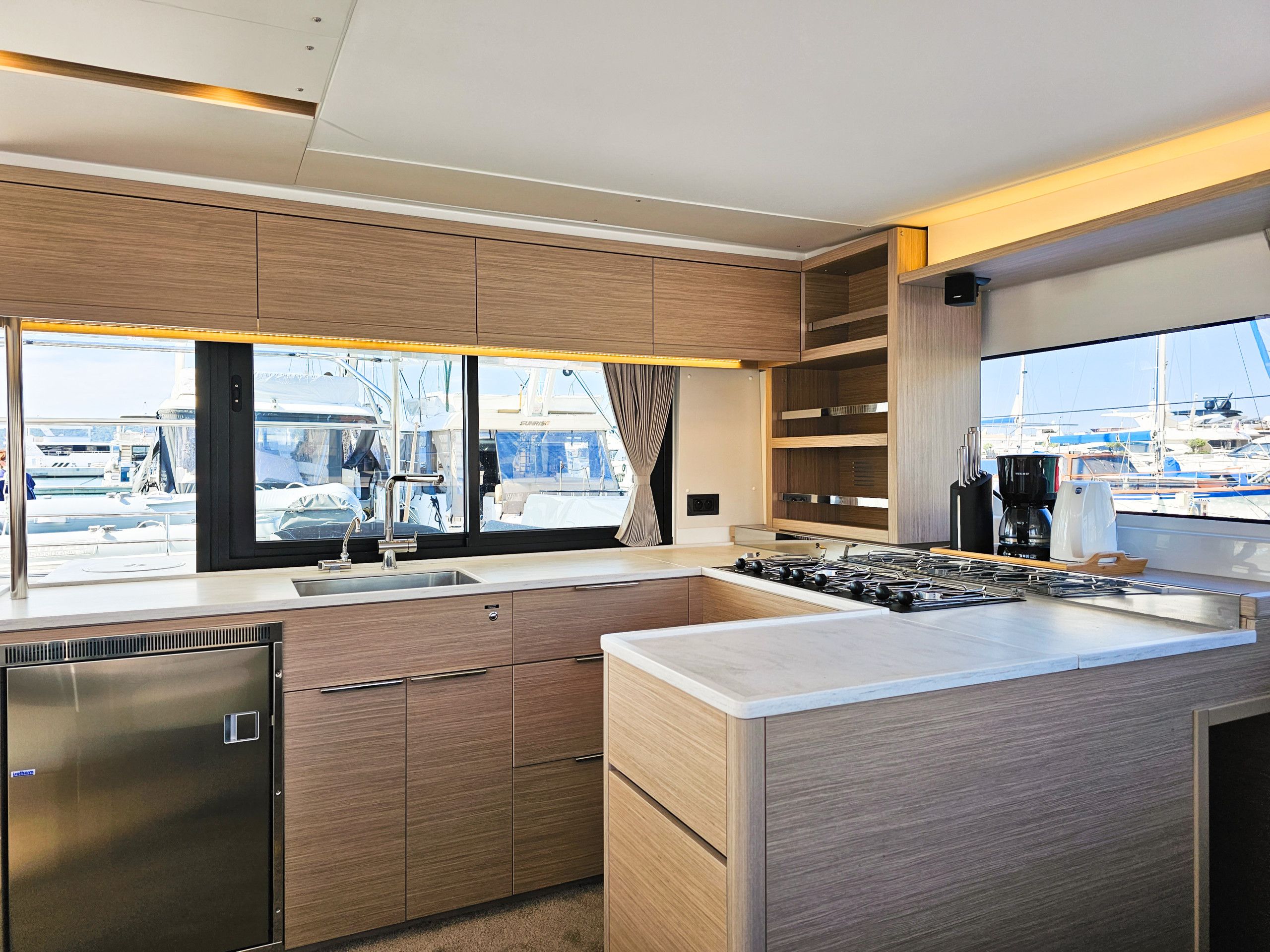 Cocina moderna con estufa integrada, electrodomésticos de acero inoxidable y un amplio ventanal con vista a un puerto deportivo.