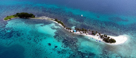 An aerial view of a tropical island with a beach, boats, and clear blue waters.