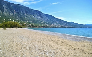 A beach with pebbles, a mountain, and houses in the background.