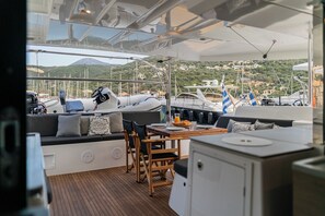 A yacht's deck with seating, a table, and a view of the marina and hills. - Sun-Kissed Sailing Adventure in the Ionian Islands, Lefkada (Lefkada)