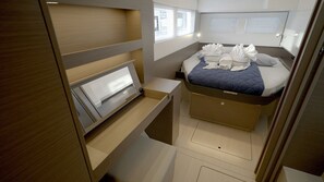 Ein kompakter, moderner Raum mit Bett, integrierten Stauraumlösungen und einem Fenster mit Jalousien.