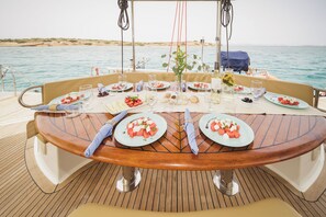 A dining table on a boat with plates of food, glasses, and a vase with flowers.