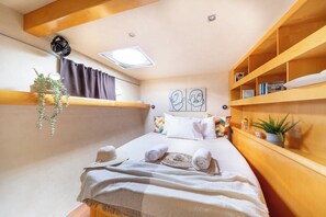Une chambre confortable avec un lit, une étagère remplie de livres, une plante suspendue et une petite fenêtre.