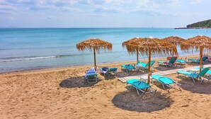 Ein Strand mit Liegestühlen und Reetsonnenhütten, ein Sandstrand und ruhiges Meer.