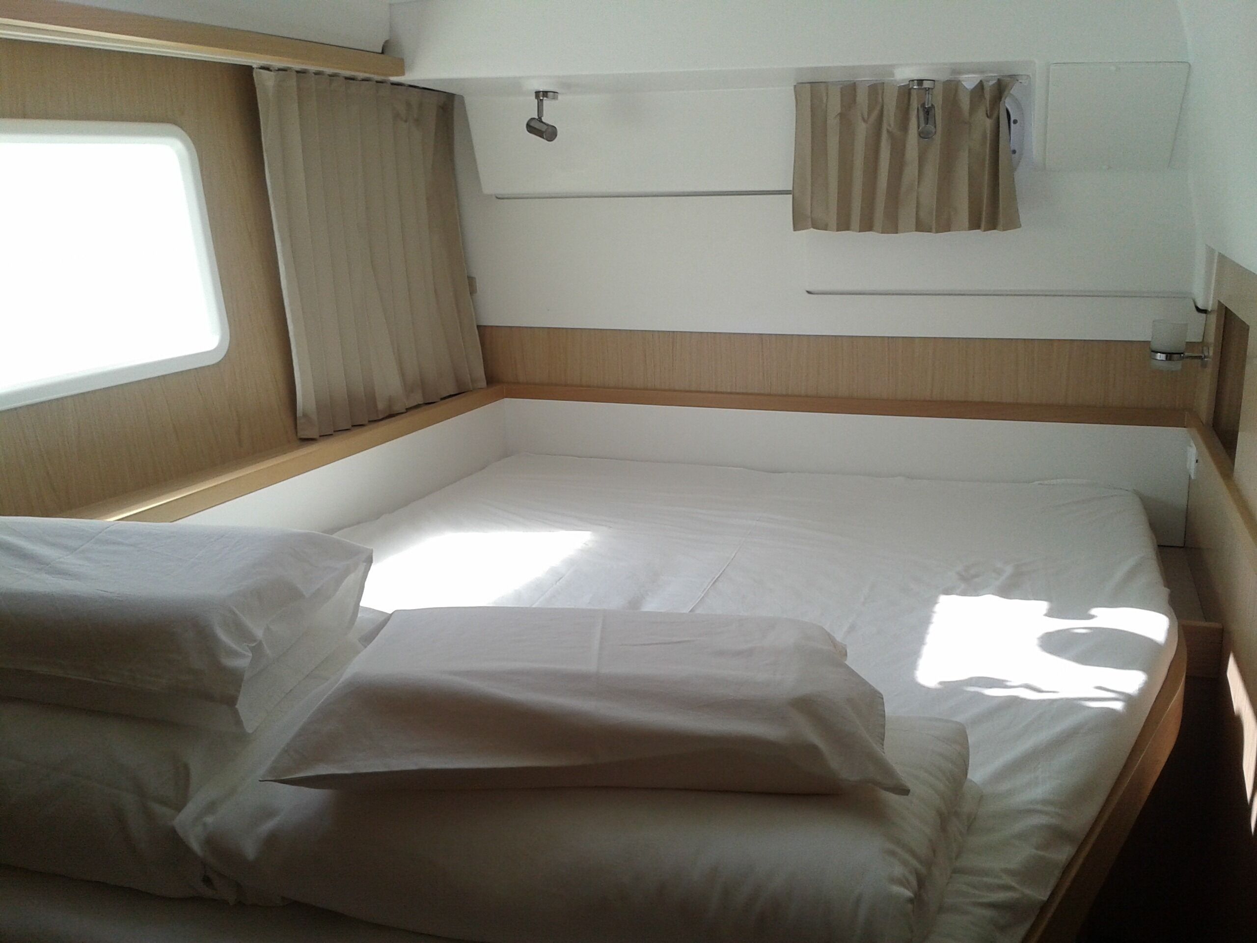 Un lit simple avec du linge de lit blanc, une fenêtre avec des rideaux et une tête de lit en bois.