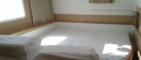 A single bed with white linens, a window with curtains, and a wooden headboard.