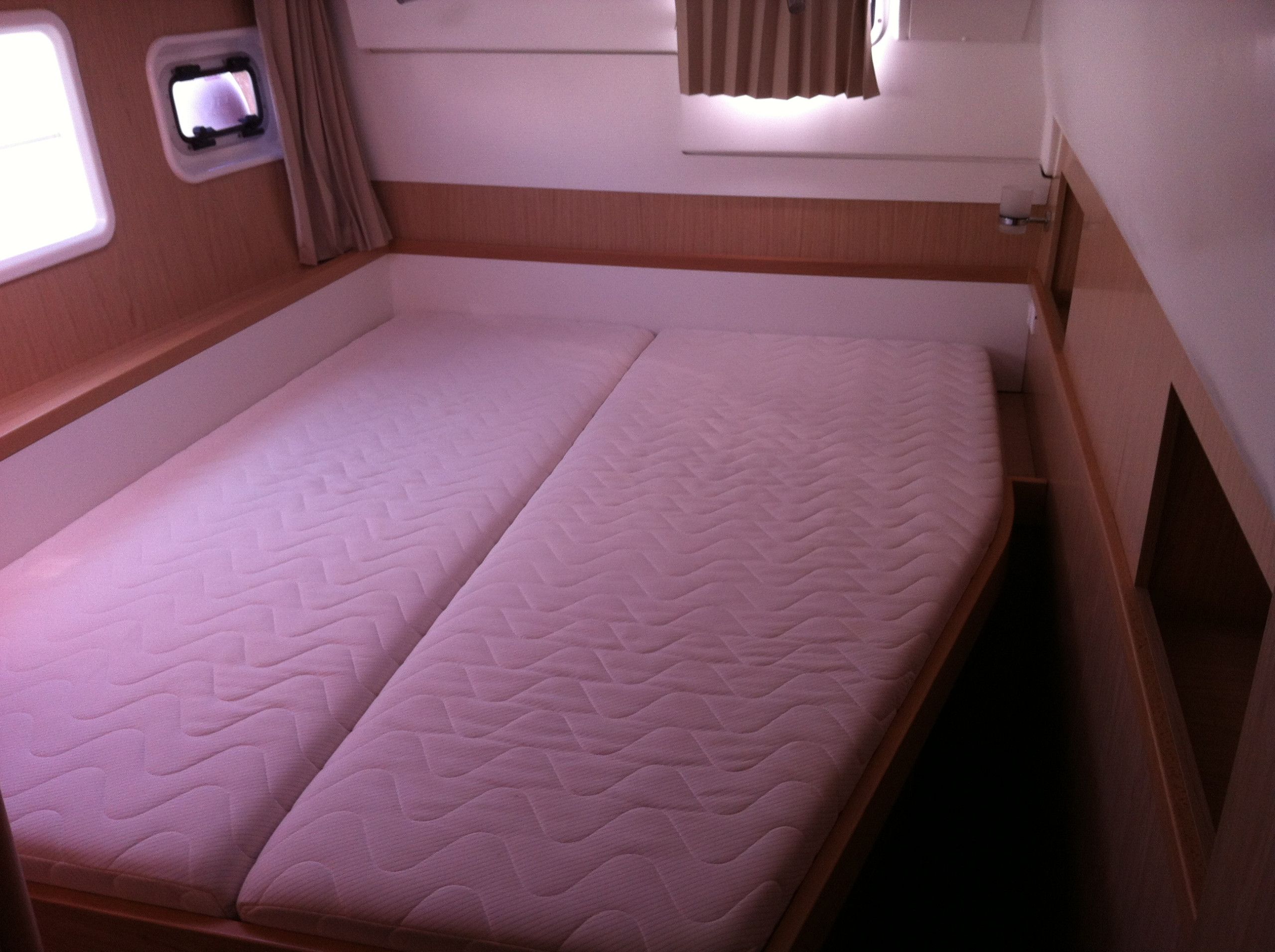 A single bed with a quilted mattress in a cabin with a window and a small shelf.