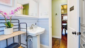 A bathroom with a white sink, a mirror, a potted orchid, and a door leading to a dining area. - Oak Cliff Oasis I Swim Spa, Sauna, & Gameroom! 10 Min to Bishop Arts District (Dallas)