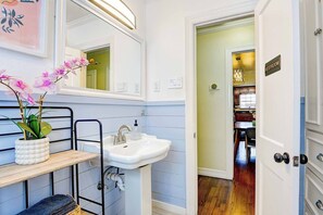 A bathroom with a white sink, a mirror, a potted orchid, and a door leading to a dining area. - Oak Cliff Oasis I Swim Spa, Sauna, & Gameroom! 10 Min to Bishop Arts District (Dallas)