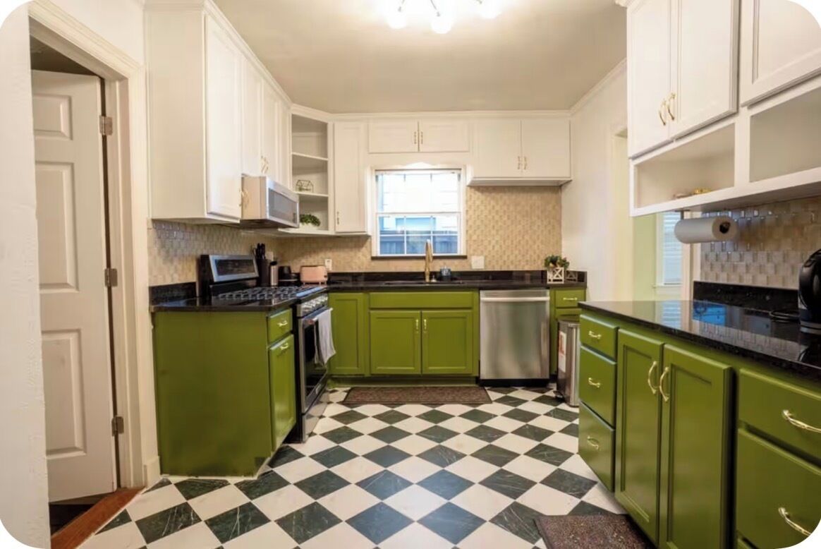 Una cocina con gabinetes verdes, piso a cuadros y paredes blancas.