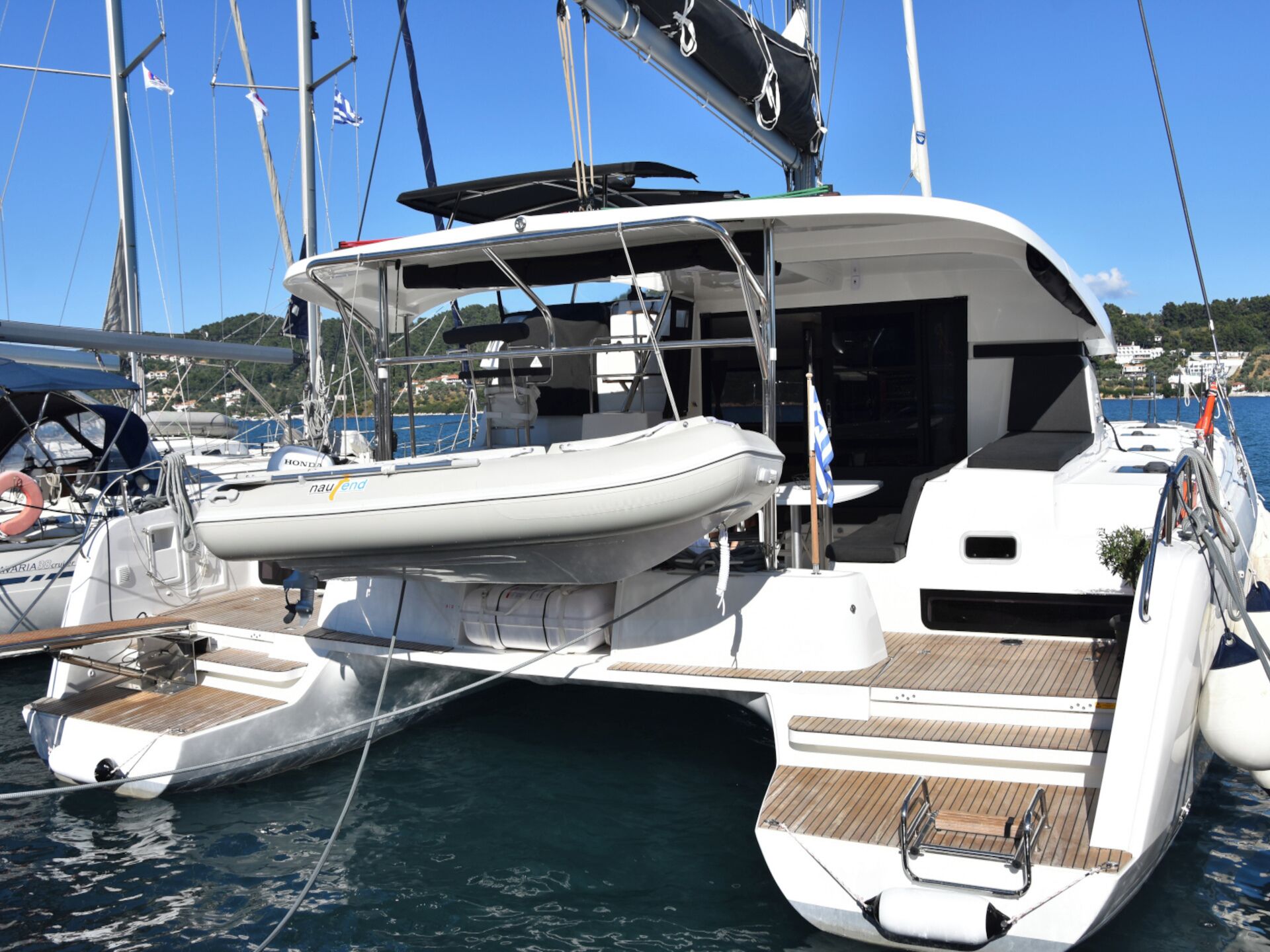 A yacht docked at a marina with a covered deck, a small boat in the foreground, and other yachts in the background.