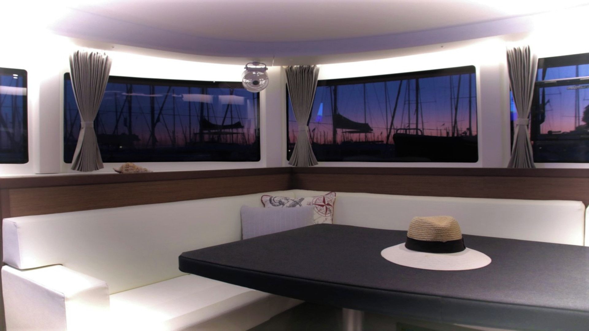 Quarto com mesa, banco, janelas amplas com cortinas e vista para o céu.