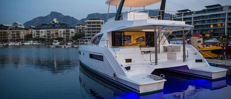 A white yacht docked at a marina with a covered deck and a view of the surrounding buildings.