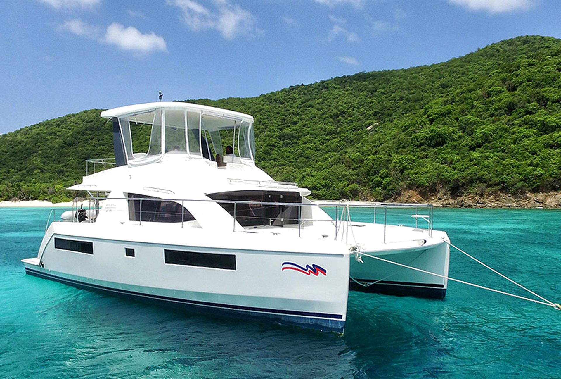 A white yacht docked in turquoise waters with a forested hill in the background.