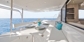 Ein Essbereich auf einem Boot mit einem für zwei Personen gedeckten Tisch, Blick aufs Meer und eine Kabine mit Fenster.