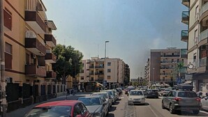 Une rue bordée d’immeubles à plusieurs étages, de voitures garées et d’un ciel dégagé.