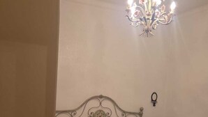 Une chambre à coucher avec un lit en métal, une table de chevet ornée d’un vase et un lustre.