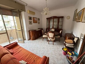 Ein Wohnzimmer mit einer Couch, einem Esstisch, Stühlen, einem Schrank und einer Deckenleuchte.