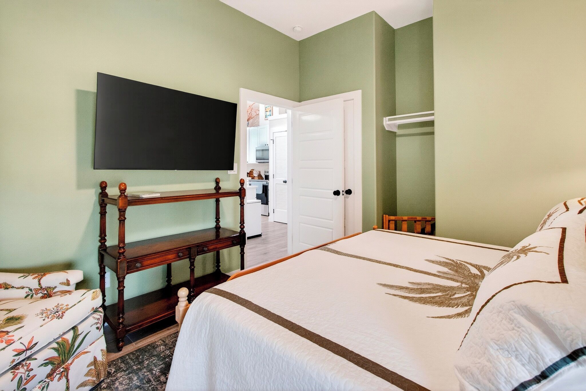 Une chambre à coucher comprenant un lit, une table de chevet en bois, un téléviseur fixé au mur et une porte donnant accès à une salle de bain.