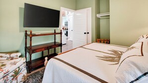 Un dormitorio con cama, una mesita de noche de madera, un televisor montado en la pared y una puerta que da al baño.