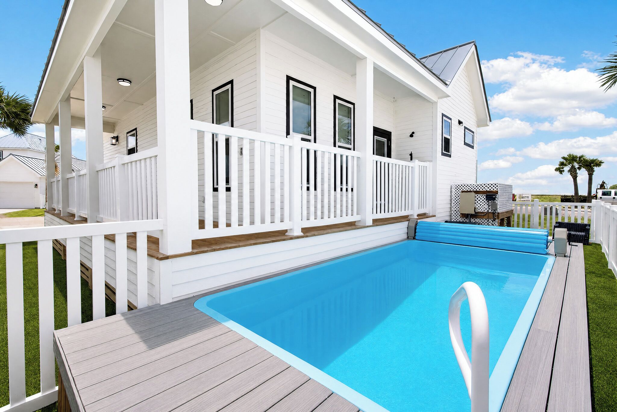 A house with a swimming pool, a covered deck, and a white fence.