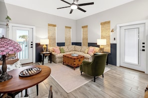 Un salon comprenant un canapé, un fauteuil vert, une table basse en bois et un ventilateur de plafond.