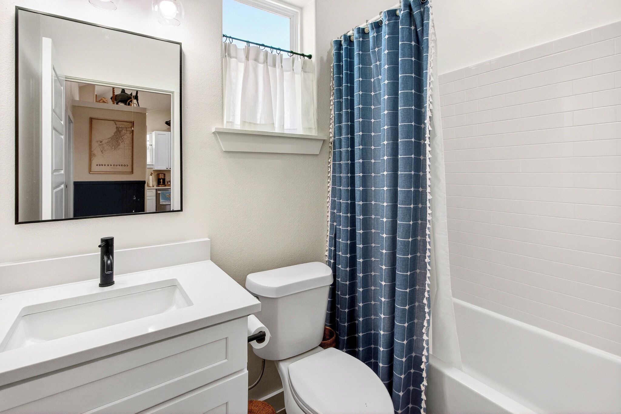 Une salle de bain avec un lavabo blanc, des toilettes, un miroir et un rideau de douche bleu.