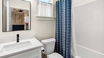 Une salle de bain avec un lavabo blanc, des toilettes, un miroir et un rideau de douche bleu.