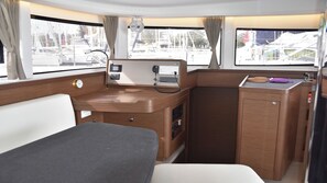 Un intérieur compact et bien éclairé, comprenant un lit, un petit bureau et une fenêtre donnant sur le port de plaisance.