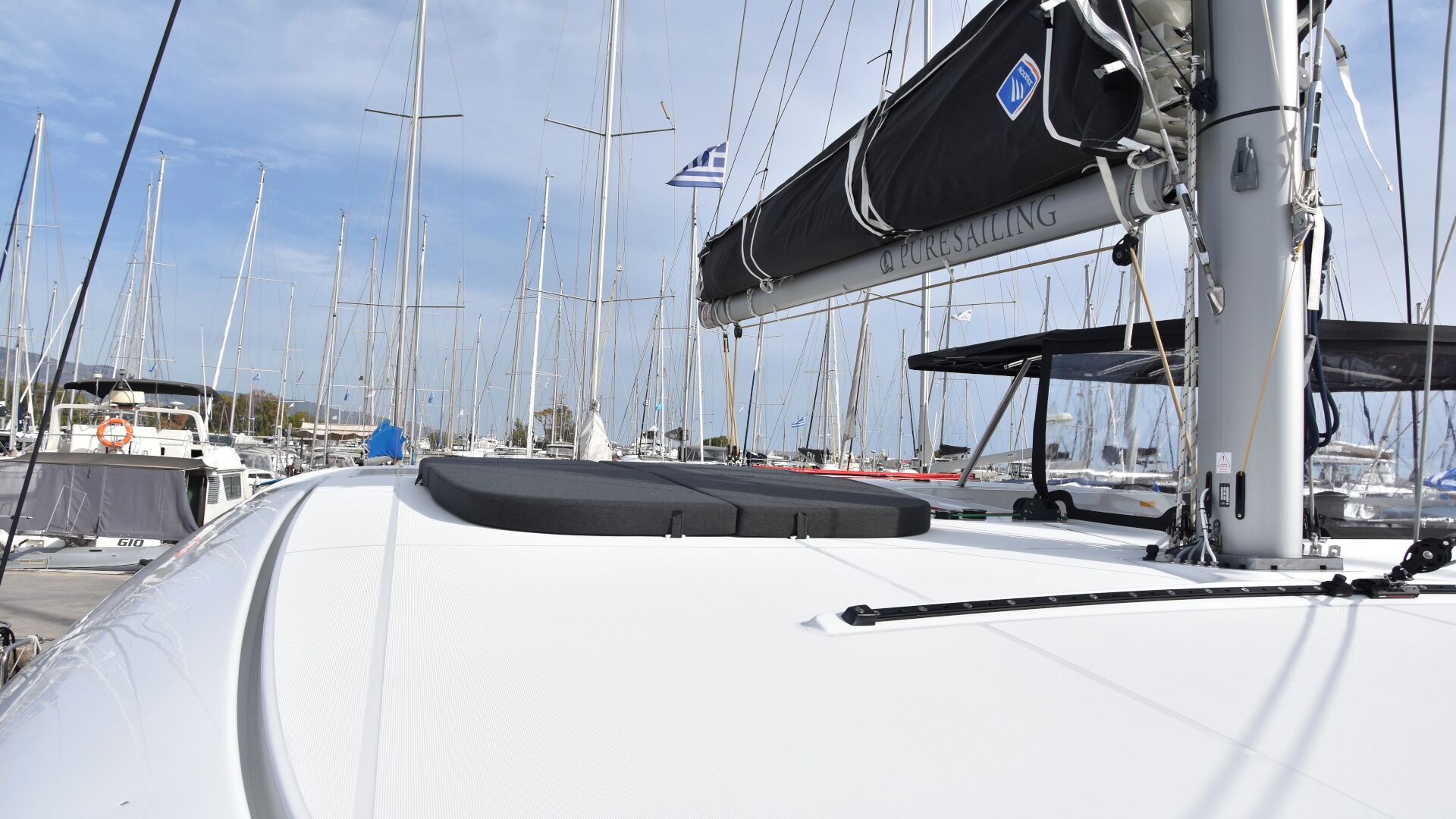 A marina with multiple sailboats docked, a covered area with a logo, and a white boat with a grey deck.