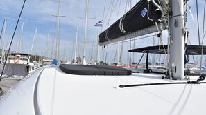 Un puerto deportivo con varios veleros amarrados, un área cubierta con un logotipo y un barco blanco con cubierta gris.
