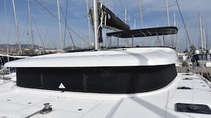 A boat's deck with a covered seating area, a mast, and multiple other boats in the background.