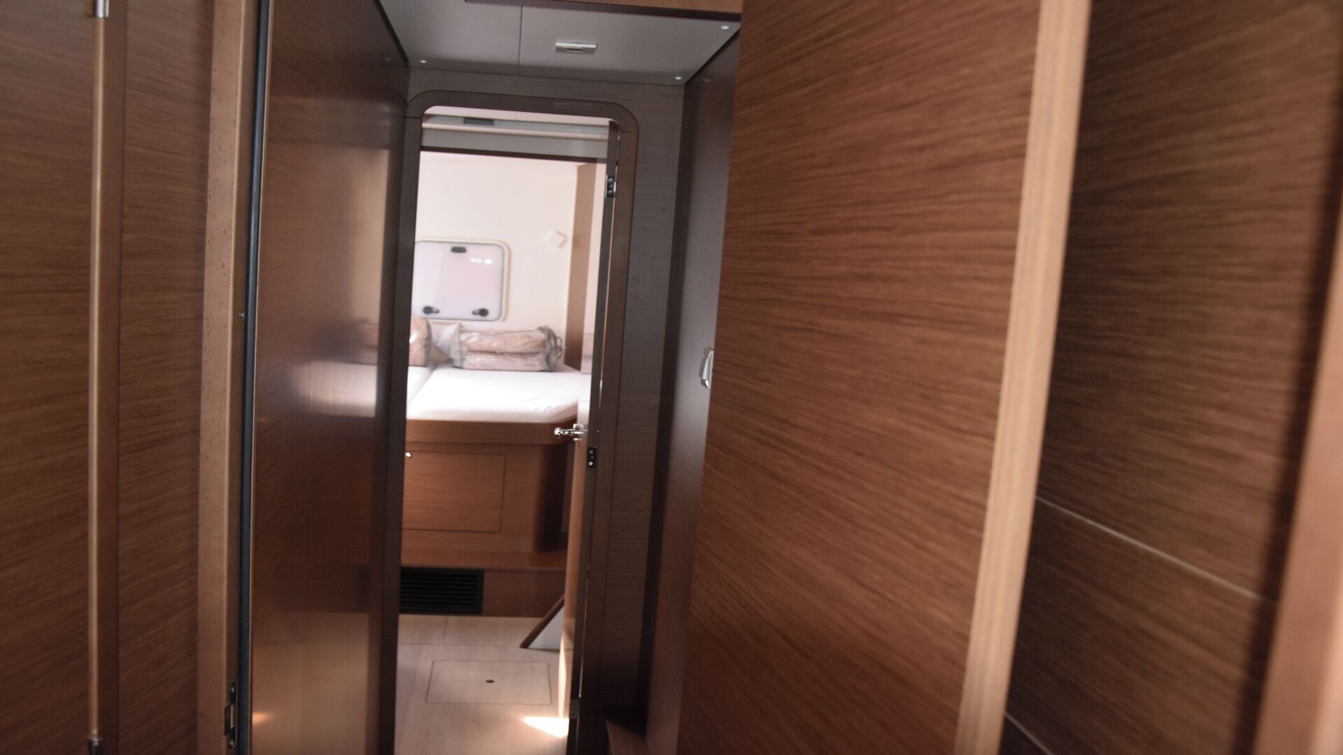 A narrow hallway leading to a bedroom with a bed and a bedside table.