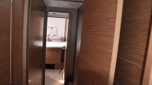 Un pasillo estrecho que lleva a un dormitorio con cama y mesita de noche.