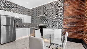 A modern kitchen with a stainless steel refrigerator, white cabinets, a patterned backsplash, and a brick wall.