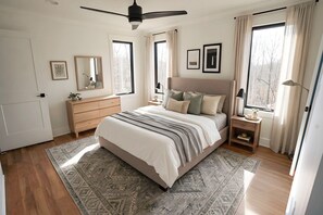 A bedroom with a bed, bedside tables, a dresser, a ceiling fan, and large windows with curtains.