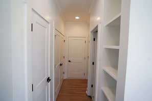 A narrow hallway with white walls, a wooden floor, and white doors with black handles. - Modern 3-bedroom Lake Retreat (Stewart)