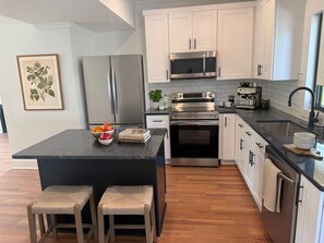 A modern kitchen with white cabinets, stainless steel appliances, a central island with stools, and a framed botanical print on the wall. - Modern 3-bedroom Lake Retreat (Stewart)