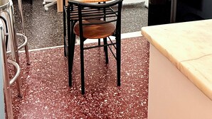 Eine kleine Küchenzeile mit Mikrowelle, Spüle und einem Holztisch mit Stühlen. An der Wand hängt ein gerahmtes Bild und es gibt einen Kleiderhaken.