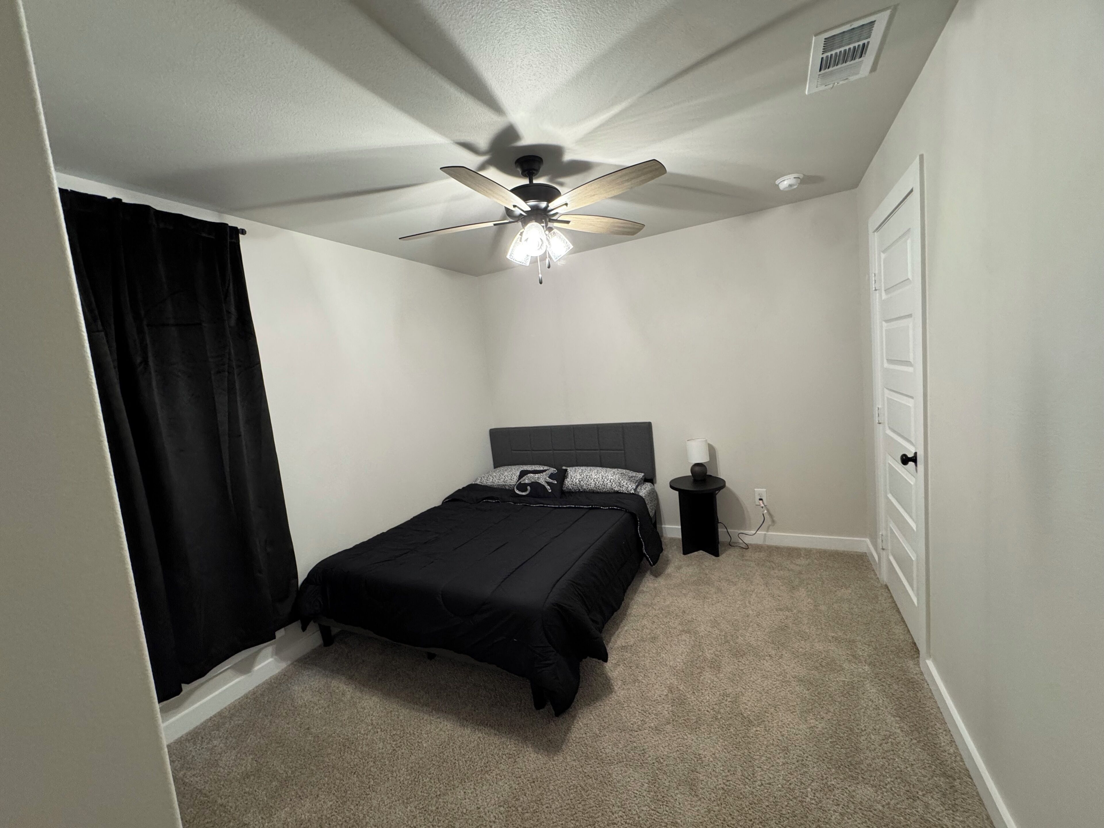 A bedroom with a bed, a ceiling fan, a nightstand, and a door.
