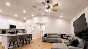 Eine moderne Küche mit einer zentralen Kochinsel, Barhocker, einem grauen Sofa und einem Deckenventilator.