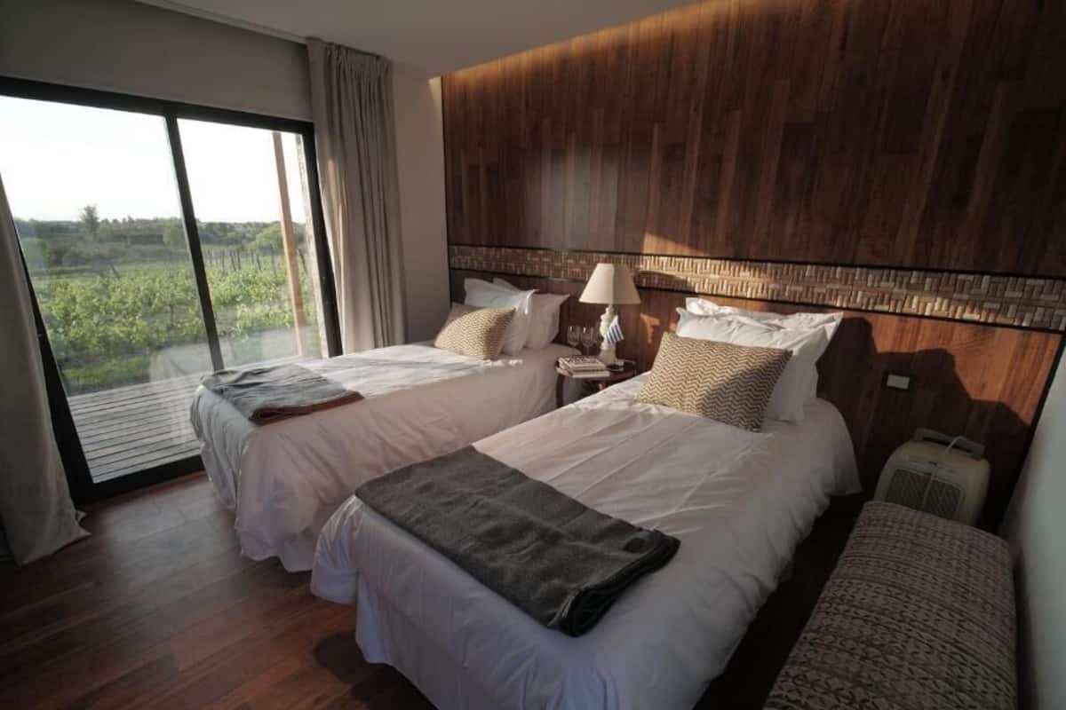Habitación de hotel con dos camas, un ventanal grande y vistas a la vegetación.