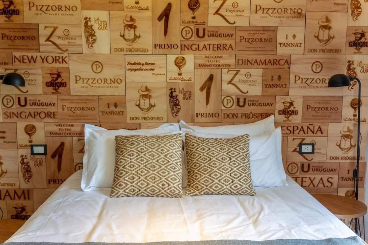 Una cama con almohadas estampadas y una pared con varios logotipos de Pizzorno.