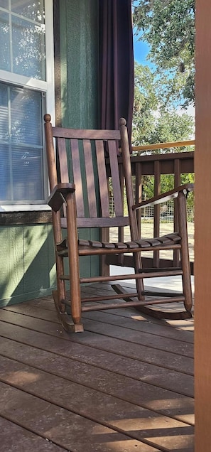 Una mecedora de madera en una terraza de madera, con una ventana y cortinas.
