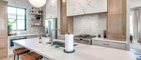A modern kitchen with a large island, stainless steel appliances, and wooden cabinetry.